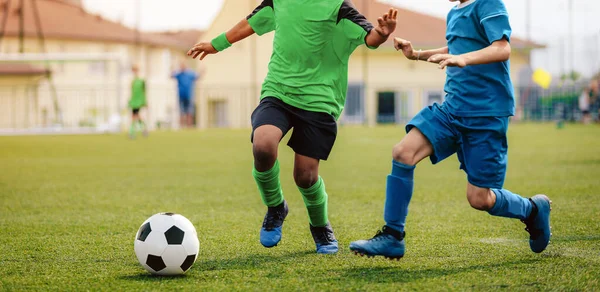 サッカー選手2人が試合でサッカーボールを蹴った 男子学生はスポーツ競技をする サッカーの試合をしている２人の多人種の子供 緑と青のサッカージャージの制服の子供たち — ストック写真