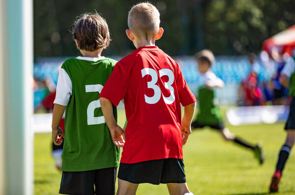 Два юноши соревнуются в спортивной игре. Дети в противостоящей команде стоят бок о бок в красных и зеленых майках Джерси. Дети в школе играют в футбол в солнечный летний день