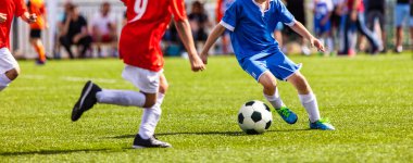 Çocuklar futbol oynar. Gençler spor sahasında futbol oynuyor. Çocuklar dışarıda futbol oynuyor. Genç erkek futbolcular kırmızı ve mavi spor üniformalarıyla koşuyorlar.