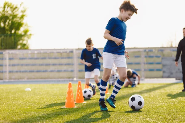 Happy Kids on Training Soccer Drill. Young European Footballers Dribbling Around Cones in Drill. Soccer Boys in Training With School Young Coach
