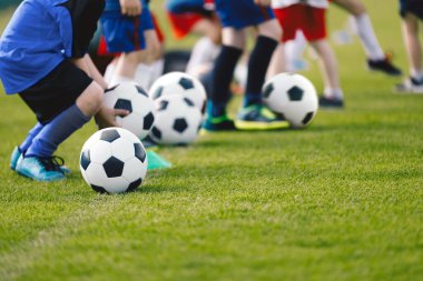 Bir grup okul çocuğu yaz kampında futbol toplarını tekmeliyor. Antrenman sınıfında futbol takımındaki çocuklar renkli kıyafetler giyiyordu. Çocuklar çim tarlasında futbol çalışıyor.