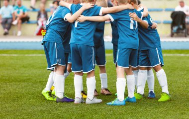 Motivated youth soccer team cheering on court. Players huddling in a circle on the field. Football captain talking to a group of soccer players. Happy football team in a circle 
