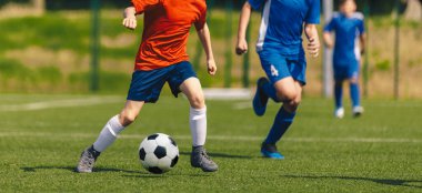 Gençler Koşu Düellosunda Turnuva Maçı. Yaz güneşli bir günde futbol maçı. Kırmızı ve Mavi formalı okul çocukları çimende klasik futbol topu koşuyor.