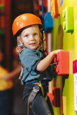 Kapalı Salon Tırmanma ve Kayalık Merkezi 'nde Kırmızı Kasklı Mutlu Okul Çocuğu. Çocuk Kameraya Gülümseyen ve Başparmağını Yukarı Tutan