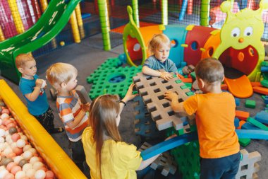 Anaokulunda eğitim grubu aktivitesi. Genç öğretmen bebek bakıcısıyla köpük bloklarıyla oynayan mutlu çocuklar.
