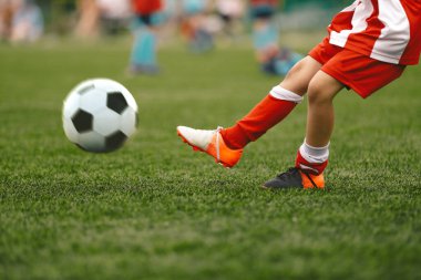 Futbolcu çim tarlasında topa vuruyor. Futbol oynanıyor. Çizgili kırmızı beyaz üniformalı okul futbolcusu.