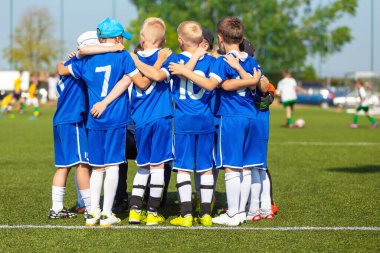 Sportif oyuncular sahada bir çember oluşturuyorlar. Sahada tezahürat yapan motive olmuş bir genç futbol takımı. Takım kaptanı bir grup futbol arkadaşıyla konuşuyor. Mavi futbol formalı mutlu futbol takımı