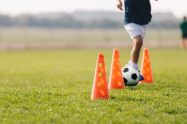 Antrenman konisi olan çocuk futbolcu. Futbol çeviklik eğitim ekipmanları. Çocuklar çim tarlasında spor yapıyor. Mutlu çocuklar spor yapar. Çocuklar futbol hız eğitim tatbikatı