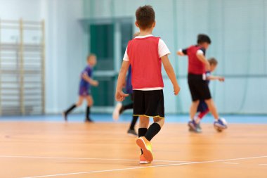 Çocuklar için futbol eğitimi. Spor salonunda futbol topuyla oynayan genç futbolcu. Spor geçmişi. İlköğretim çağındaki çocuklar kapalı alanda futbol oynuyor.