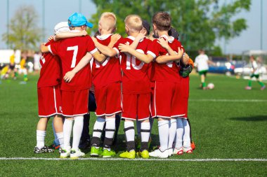 Sportif oyuncular sahada bir çember oluşturuyorlar. Sahada tezahürat yapan motive olmuş bir genç futbol takımı. Takım kaptanı bir grup futbol arkadaşıyla konuşuyor. Kırmızı futbol formalı mutlu futbol takımı.
