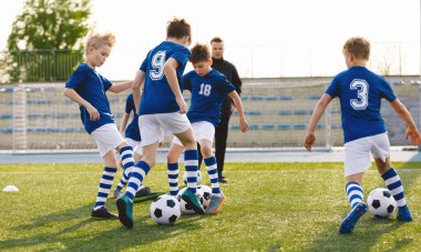 Happy Kids on Training Soccer Drill. Young European Footballers Dribbling Balls. Soccer Boys in Training With School Young Coach