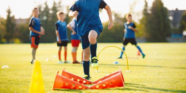 School kids jumping over obstacles on the training pitch. Group of children in sports soccer training. Boys improving agility skills on sport class