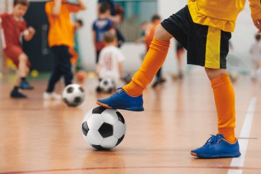 Çocuklar için futbol futsal eğitimi. Futbol antrenmanı. Spor salonunda futbol topuyla oynayan genç futbolcu. Sarı üniformalı bir oyuncu. Spor arkaplanı