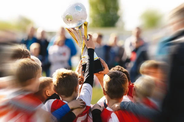 Victory celebration of a youth sports team. Happy kids winning sports tournament. Schoolboys standing in a circle and holding the golden trophy