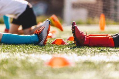 İki spor takımındaki çocuklar. Antrenman maçında iki futbolcunun bacakları çimlere oturur. Beden eğitimi dersinde spor yapan çocuklar
