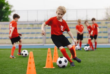 Futbol antrenmanındaki çocuklar. Genç oyuncular antrenman konilerinin arasına top sürüyor. Futbol yaz kampı. Futbol antrenmanındaki oyuncular