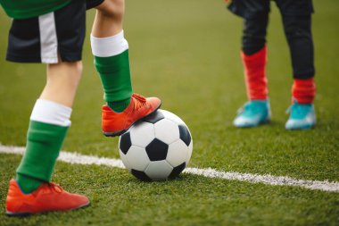 Futbol oyuncusunun bacakları klasik futbol topunu tekmeliyor. Eğitim Sahasında Futbol Çalışması Yapan Okul Çocukları