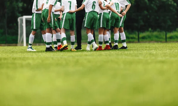 Players huddling in a circle on the field. Happy football team. Motivated youth soccer team cheering on court. Coach talking to a group of soccer players.