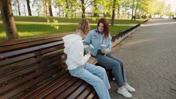 Máma a dcera měli malý piknik na lavičce v parku. — Stock video