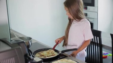 Çocuk mutfakta krep pişiriyor.