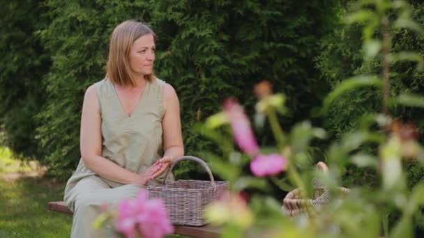 Egy nő ül egy padon a kertben — Stock videók