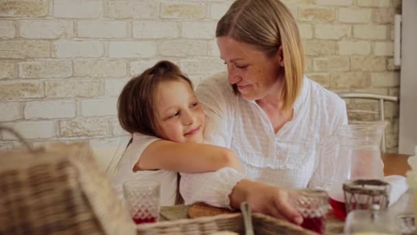 Glimlachende dochter omarmen moeder terwijl het hebben van voedsel aan tafel — Stockvideo