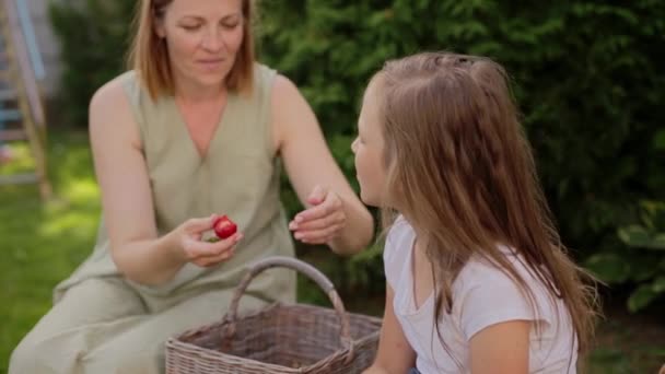 Smiling mother feeding strawberry to daughter in backyard — Stock Video