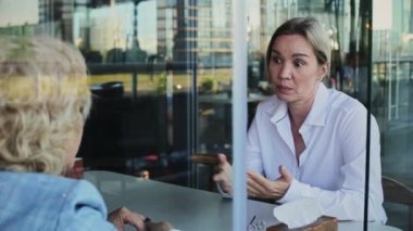 İş kadınları, cam pencereden görünen bir kafede otururken tartışıyor.