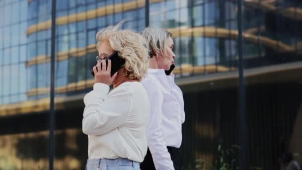 Geschäftsfrauen telefonieren beim Gang durch Bürogebäude mit Mobiltelefonen — Stockvideo