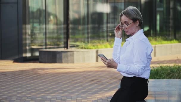 Sonriente mujer profesional hablando en el teléfono inteligente fuera del edificio de oficinas — Vídeos de Stock