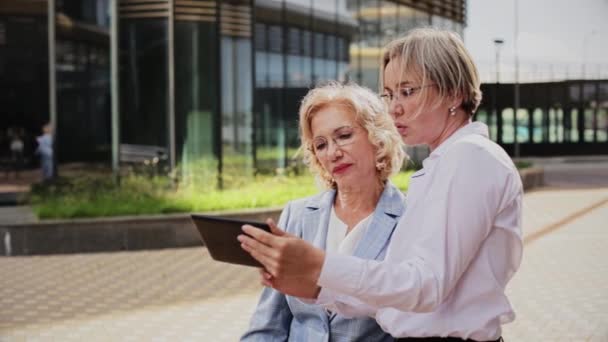 Compañeras discutiendo sobre tableta mientras están de pie fuera del edificio de oficinas — Vídeos de Stock