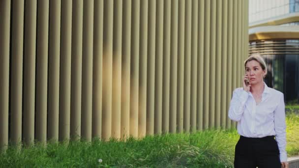 Sonriente mujer profesional hablando en el teléfono inteligente fuera del edificio de oficinas — Vídeos de Stock