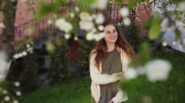 Güzel genç bir kadın bahar bahçesinde çiçek açan bir elma ağacının altında duruyor.