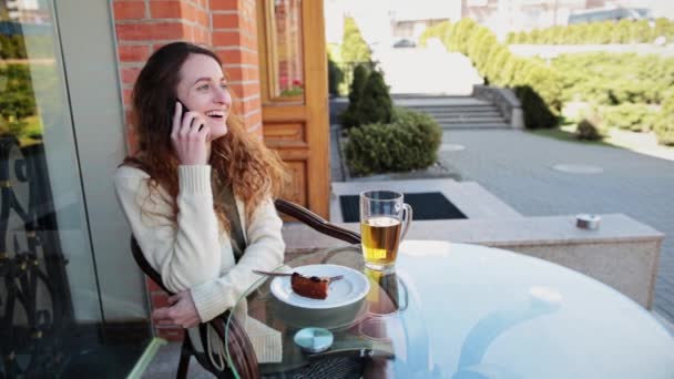 Tyttö istuu kahvilassa kadulla puhumassa puhelimessa. — kuvapankkivideo