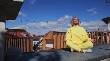 Gülümseyen orta yaşlı kadın gözleri kapalı çatıda meditasyon yapıyor.