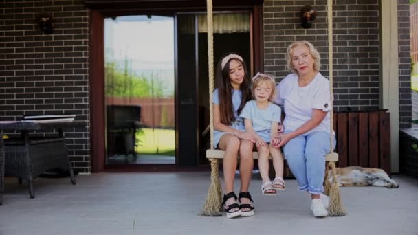 Glimlachende oma met kleindochters zittend op touw swing — Stockvideo