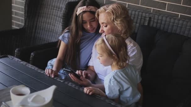 Abuela compartiendo teléfono inteligente con nietas en el sofá — Vídeos de Stock