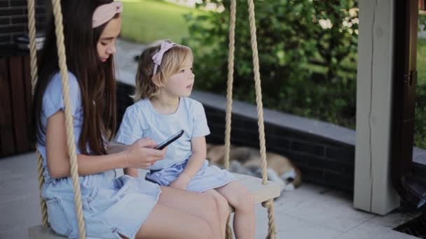 女の子共有スマートフォンとともに姉妹でパティオ — ストック動画