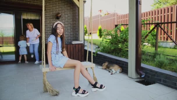 Onnellinen tyttö istuu keinu terassilla — kuvapankkivideo