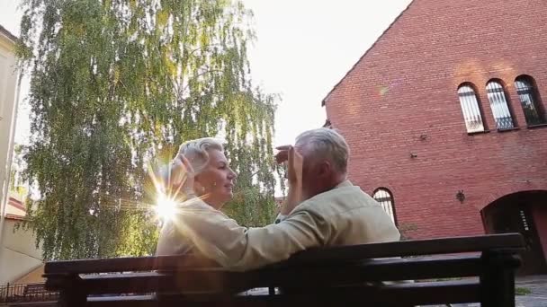 Senior kvinna sitter på bänken drar på mans näsa — Stockvideo