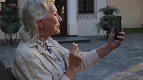 Starší žena mluví na chytrý telefon, zatímco sedí na lavičce — Stock video