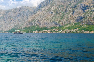 Turist teknesi, canlı mavi deniz ve etkileyici bir dağ sırası.