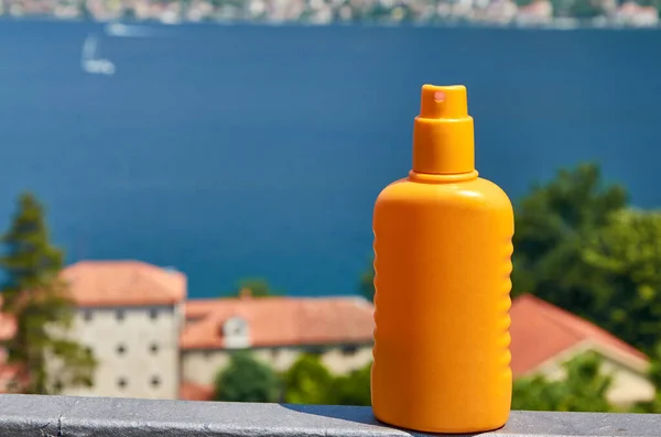 Orange bottle of a sun lotion spray with a sea in a background