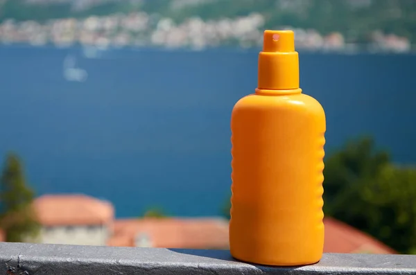 Orange bottle of a sun lotion spray with a sea in a background