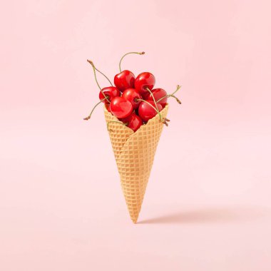 Pastel pembe arka planda taze kırmızı kirazlarla dolu dondurma külahlı yaratıcı kompozisyon. Vejetaryen tatlı konsepti.