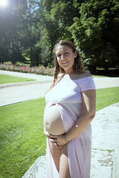 7ヶ月のピンクの透明なドレスを腹を保持妊婦 自然背景 — ストック写真