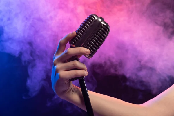 Närbild bild av scenen mikrofon i kvinnliga händer isolerad över lutning blå lila bakgrund i neon ljus med scenen rök. Resultat — Stockfoto
