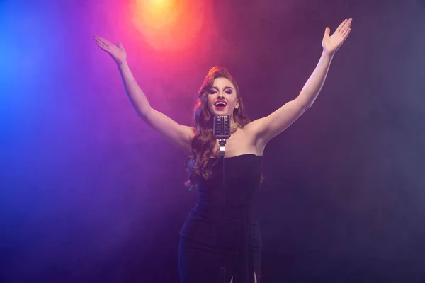 Cropped beeld van mooie getalenteerde podium zanger geïsoleerd over gradiënt blauw paarse achtergrond in neon licht met podium rook — Stockfoto