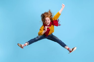 Mavi arka planda izole bir şekilde atlayan heyecanlı genç kızın yatay portresi. Bir bacadan iyileşiyor, soğuk.