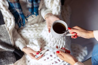 Evde izole edilmiş ve hasta hisseden iki kadının görüntüsü. Kız bardağı, termometre ve burun spreyi tutuyor.